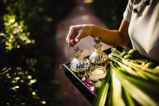 Plan rapproché grand angle de la femme tenant plateau avec des bouteilles en verre, bougie et fruits . — Photo de stock