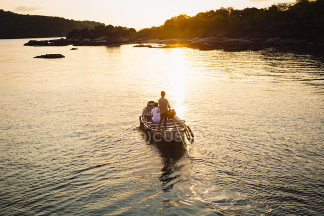 Hochwinkelaufnahme von Männern, die bei Sonnenaufgang ein kleines Boot in Richtung Insel steuern, bai tu long, vietnam. — Stockfoto