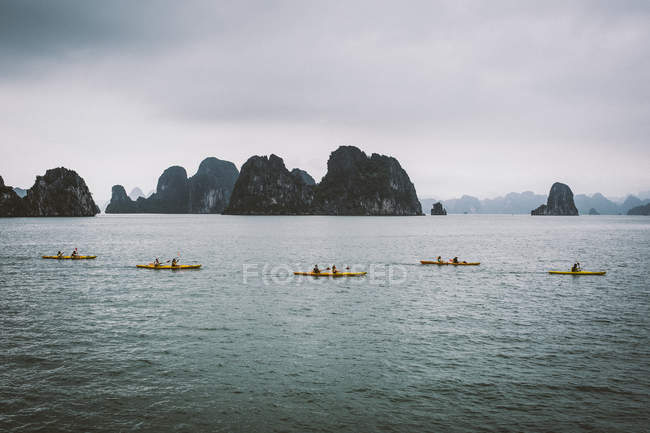 Kajakfahrer rudern in einer Bucht inmitten von Kalksteinkarstformationen, bai tu long, Vietnam. — Stockfoto