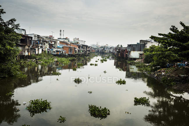 Paisaje a lo largo de un pequeño canal con casas construidas sobre el agua, Ciudad Ho Chi Minh, Vietnam . - foto de stock