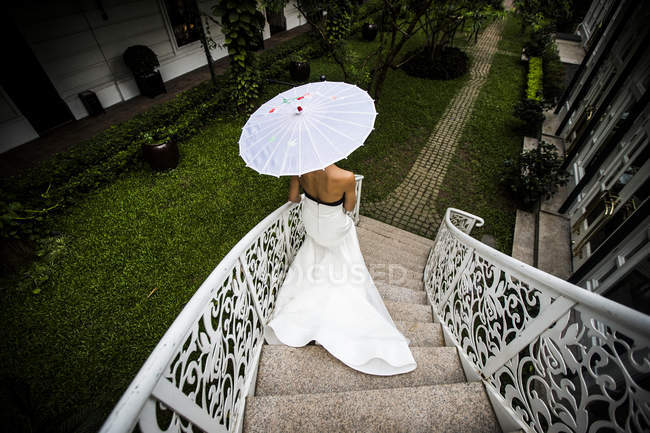 High angle view of young bride walking down an ornate staircase, obscured face with umbrella, Hanoi, Vietnam. — Stock Photo