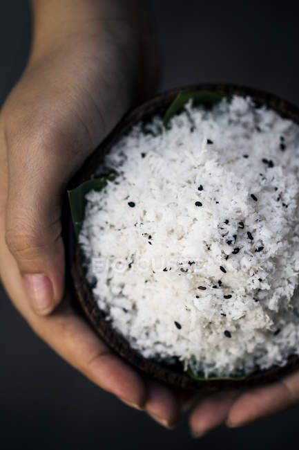 High angle close-up of hands holding bowl of coconut and black sesame seeds body scrub. — Stock Photo