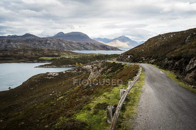 Paisagem com estrada rural cortando montanhas e loch sob um céu nublado, Western Highlands, Escócia, Reino Unido — Fotografia de Stock