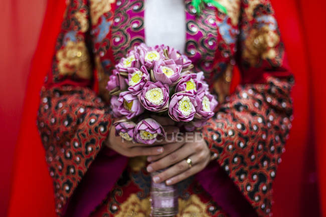Close-up de noiva vietnamita vestindo um manto colorido, segurando um buquê de flores de lótus . — Fotografia de Stock