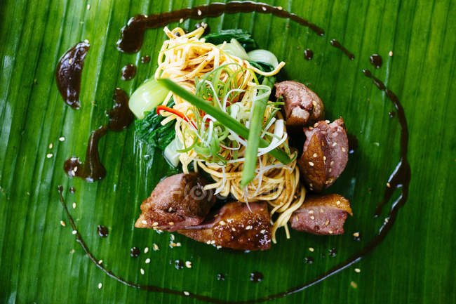High angle view of seared duck breast and noodles served on a banana leaf. — Stock Photo