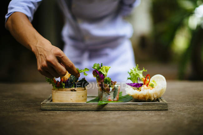 Close-up of chef putting final touch on dishes of salad and spring rolls. — Stock Photo