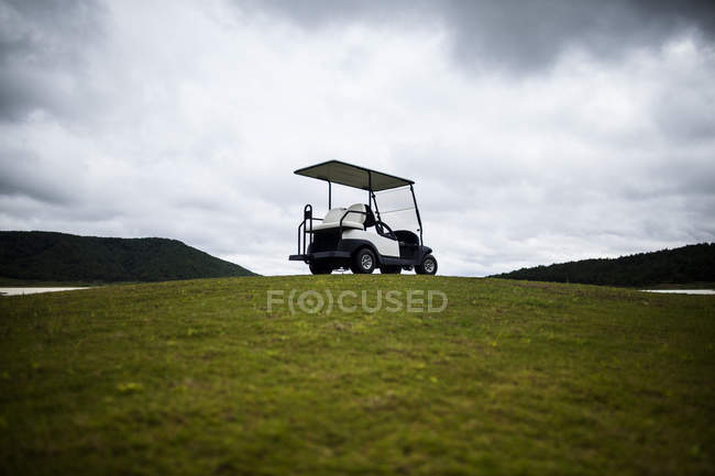 Carro de golf estacionado en la hierba verde del campo de golf bajo el cielo nublado, Dalat, Vietnam - foto de stock