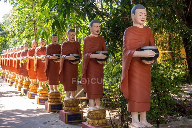 Row of Buddhist monk statues with red robes and alms bowls in garden of Buddhist temple at Siem Reap, Cambodia — Stock Photo