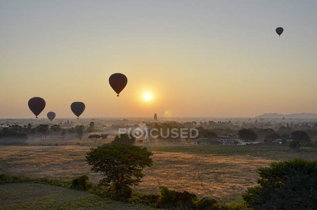 Hot air balloons over landscape with distant temples at sunset, Bagan, Myanmar. — Stock Photo