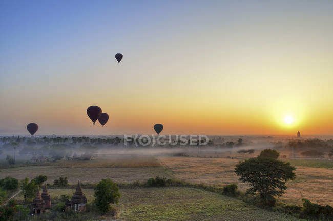 Heißluftballons über Landschaft mit weit entfernten Tempeln bei Sonnenuntergang, bagan, myanmar. — Stockfoto