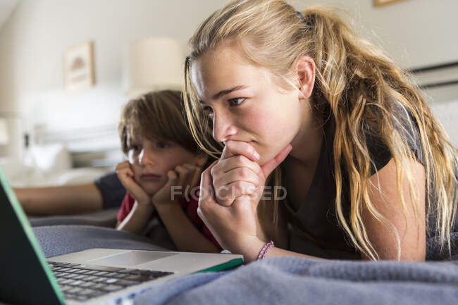 La sœur de 13 ans et son frère regardent un ordinateur portable au lit — Photo de stock