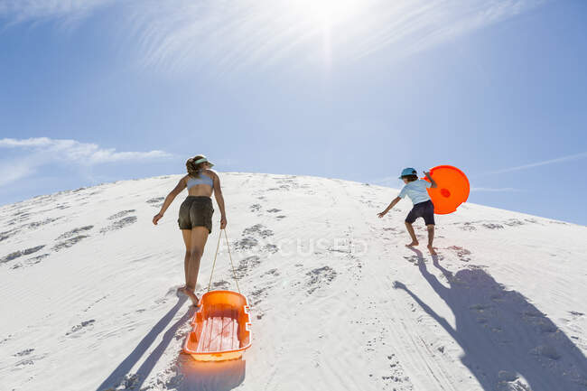 Niños con trineos y dunas de arena trepadora, Monumento Nacional de las Tierras Blancas, NM. - foto de stock