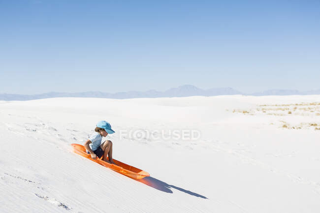 6-летний мальчик катается на санках по песчаной дюне — стоковое фото