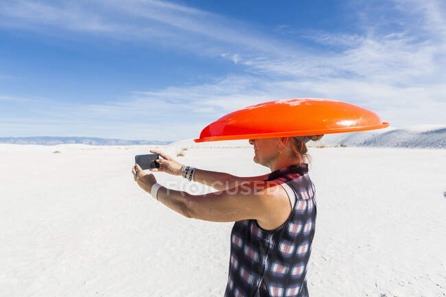 Frau mit orangefarbenem Schlitten auf dem Kopf, macht Selfie, White Sands National Monument, NM — Stockfoto