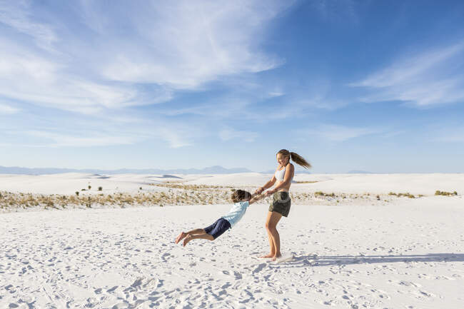Teen girl swinging suo 6 anno vecchio fratello in sabbia, White Sands Na'l Monument, NM — Foto stock