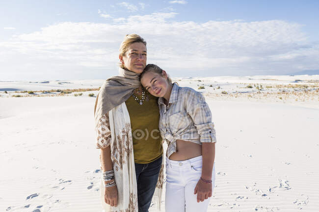 Una madre y su hija adolescente codo a codo, brazos alrededor de cineastas, en un espacio abierto. - foto de stock