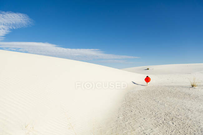 6 year old boy carrying an orange sled in a white undulating dune landscape. — Stock Photo