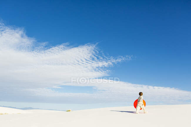 6-jähriger Junge mit orangefarbenem Schlitten in einer weißen hügeligen Dünenlandschaft. — Stockfoto