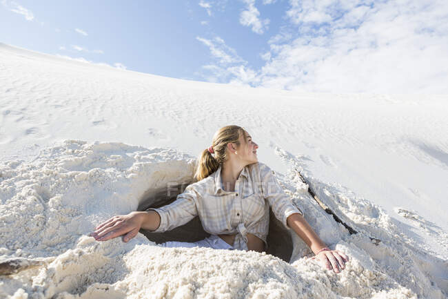 13 year old girl emerging from a dug out hole in white sand dunes. — Stock Photo