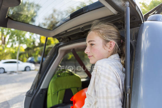 Niña de 13 años en la parte trasera del SUV con equipaje. - foto de stock