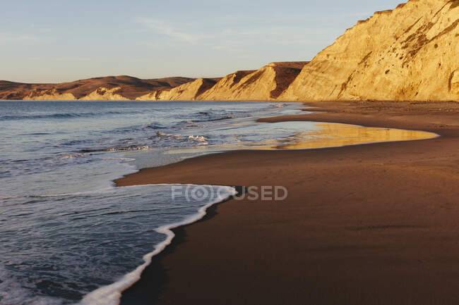 Praia ao amanhecer, com penhascos e rochas . — Fotografia de Stock