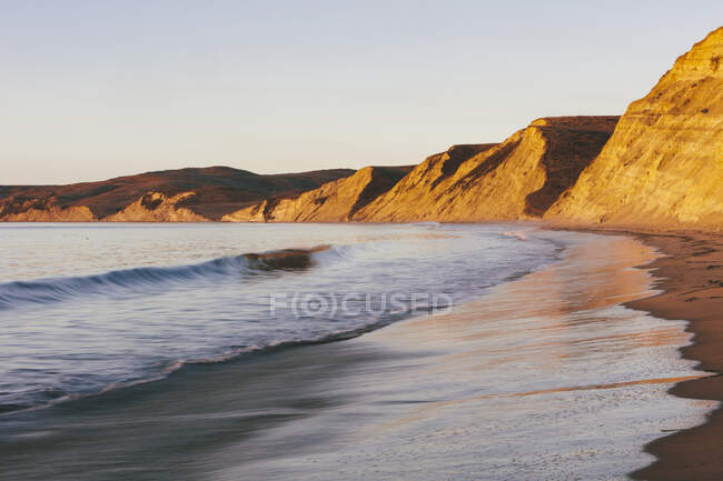 Acantilados empinados y playa con surf al amanecer - foto de stock