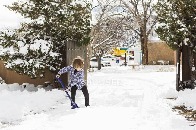 Un garçon de six ans pellete de la neige dans une allée — Photo de stock