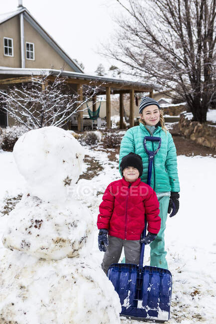 Portrait of thirteen year old teenage girl and her 6 year old brother posing with snowman — Stock Photo