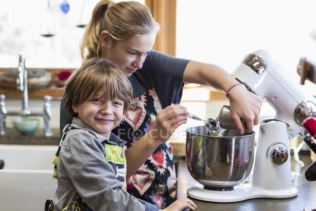 Thirteen year old teenage girl and her 6 year old brother in the kitchen,using a mixing bowl — Stock Photo