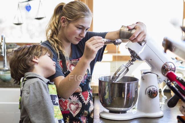 Une adolescente de 13 ans et son frère de 6 ans dans la cuisine, à l'aide d'un bol de mélange — Photo de stock