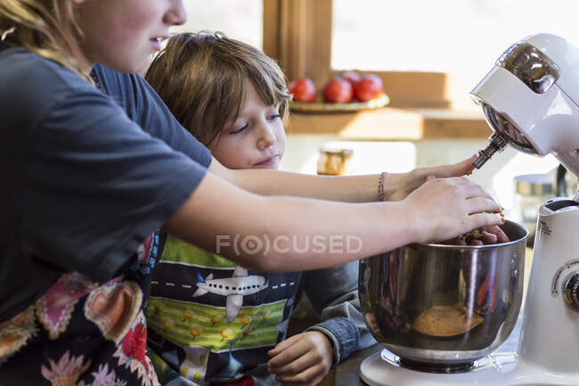 Tredici anni ragazza adolescente e suo fratello di 6 anni in cucina utilizzando una ciotola di miscelazione — Foto stock