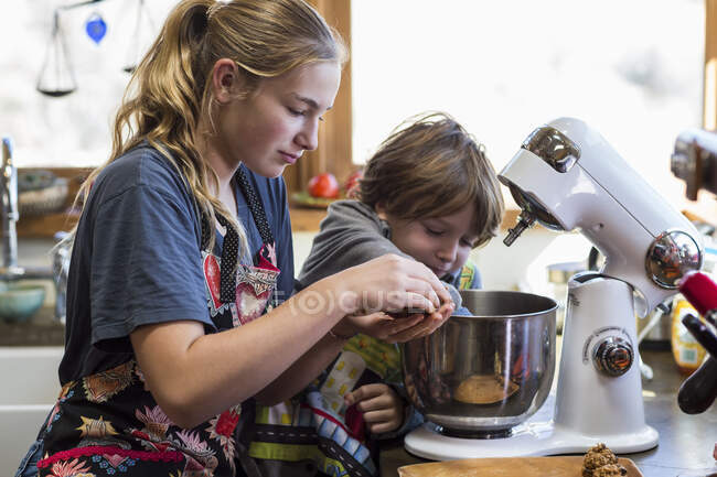 Adolescente de treze anos e seu irmão de 6 anos na cozinha, usando uma tigela de mistura — Fotografia de Stock