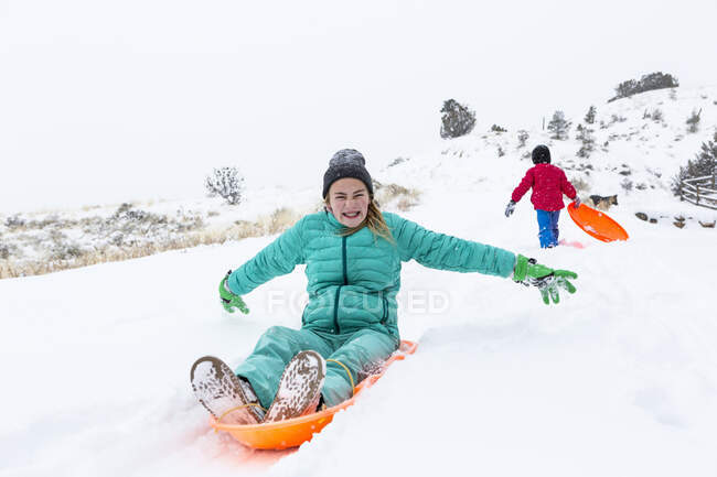 Happy siblings sledding down hill at wintertime — Stock Photo