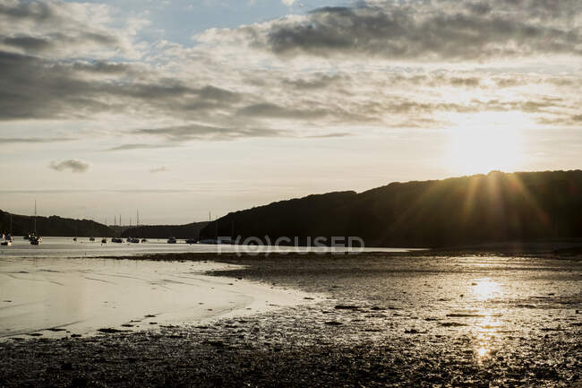 Vista su una spiaggia sabbiosa verso barche a vela e scogliere lontane al tramonto . — Foto stock