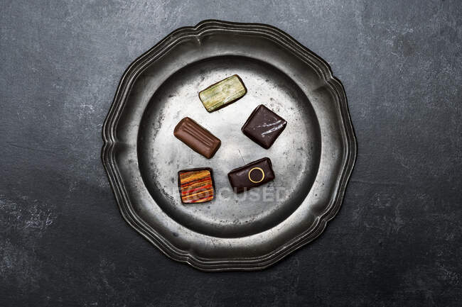 Alto angolo da vicino di una selezione di praline al cioccolato su un piatto di latta su sfondo nero . — Foto stock