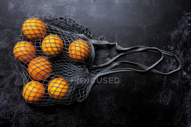 Hohe Nahaufnahme von Orangen im grauen Netzbeutel auf schwarzem Hintergrund. — Stockfoto