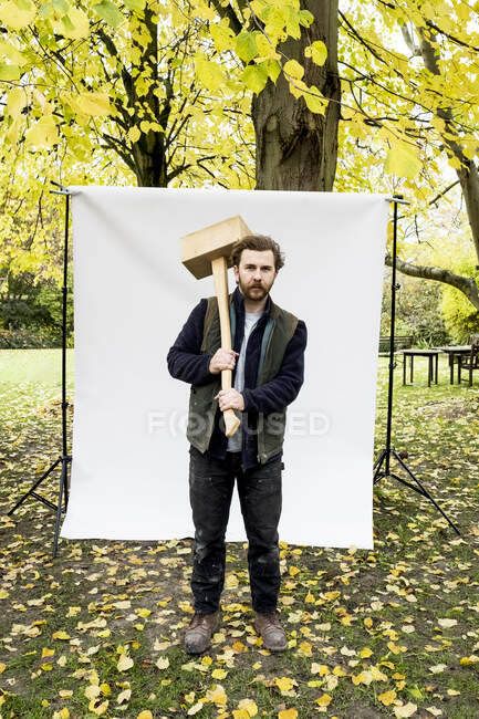Портрет бородатого чоловіка, що тримає дерев'яний блок, стоїть перед білим тлом в саду, дивлячись на камеру . — стокове фото