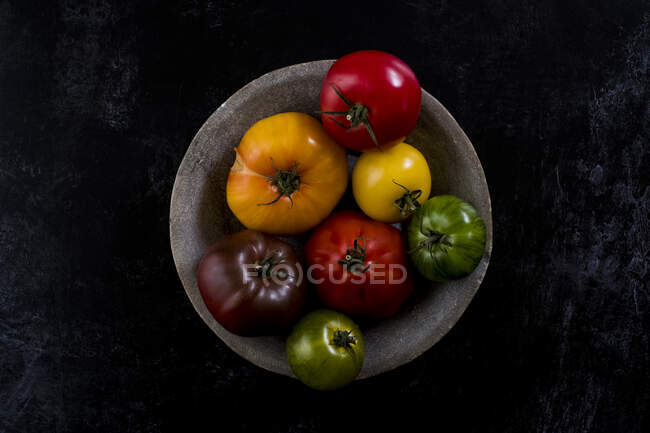 High angle close up of grey plate with selection of tomatoes in various shapes and colours on black background. — Stock Photo