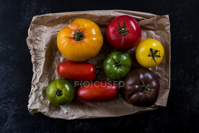 High angle close up of a selection of tomatoes in various shapes and colours on black background. — Stock Photo