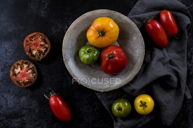 High angle close up of grey plate and cloth and a selection of fresh tomatoes on black background. — Stock Photo