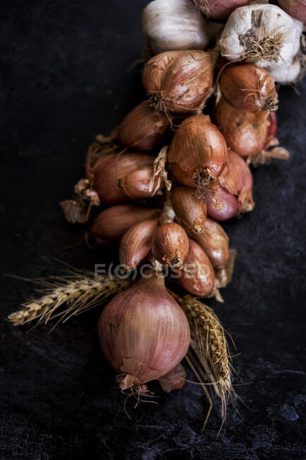 Alto angolo primo piano di stringa di cipolle e aglio su sfondo nero . — Foto stock