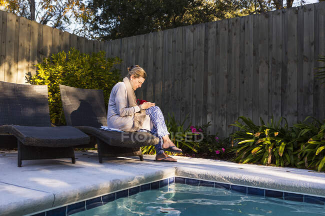 Femme assise sur une chaise longue près d'une piscine — Photo de stock