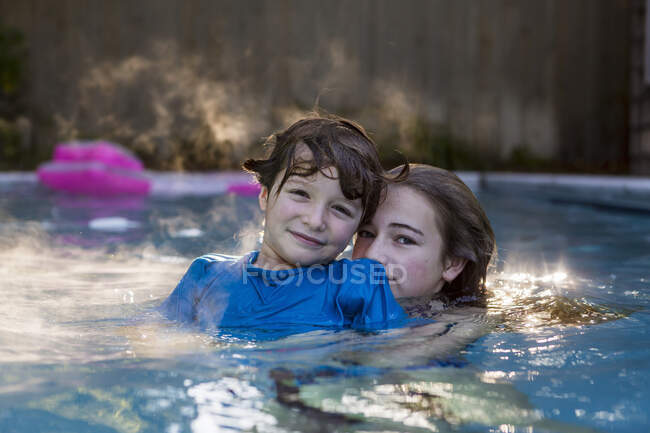 Los hermanos jugando en la piscina a la luz de la madrugada - foto de stock