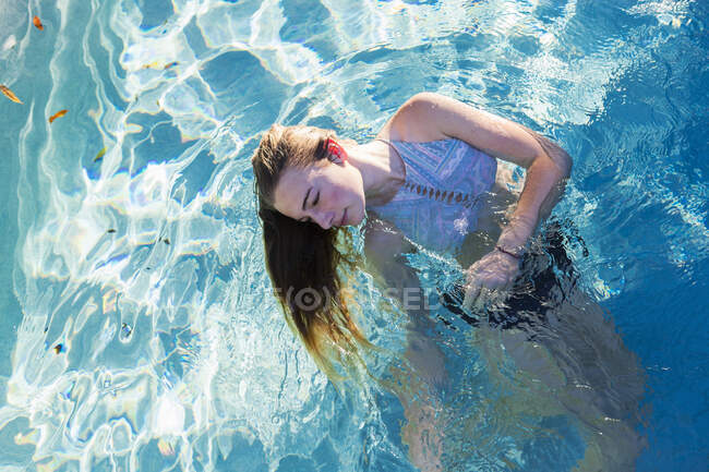 Niña adolescente nadando en una piscina, devuelva el cabello flotando en el agua.. - foto de stock
