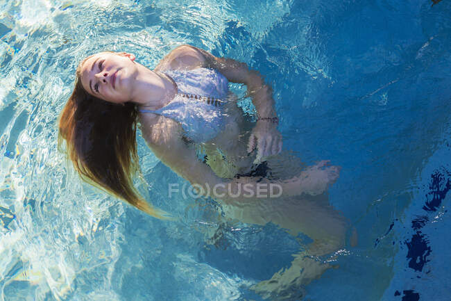 Дівчина-підліток плаває в басейні, плаваюча голова спини волосся поширюється на воді . — стокове фото
