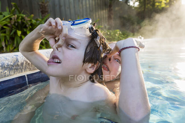 Niño y su hermana jugando en la piscina a la luz de la mañana temprano, el niño sosteniendo la nariz.. - foto de stock