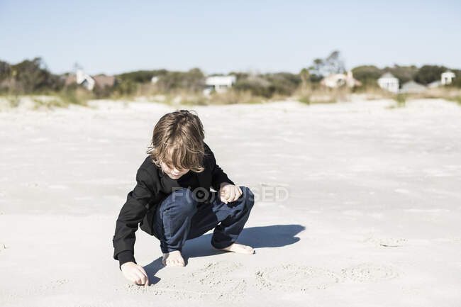 Шестирічний хлопчик малює в м'якому білому піску на пляжі — стокове фото