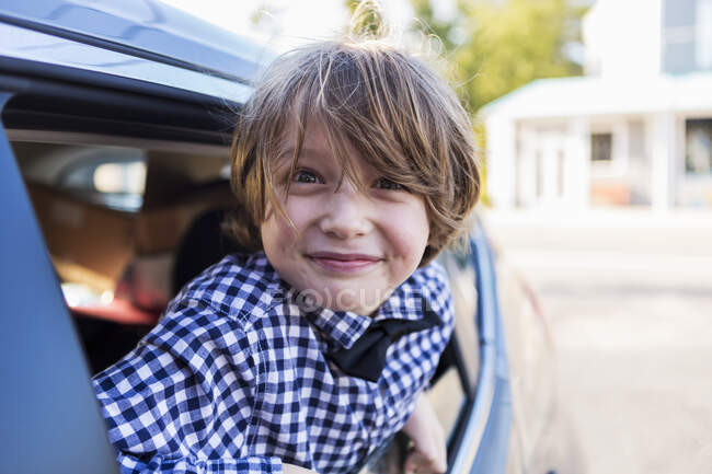 A six year old boy smiling at camera, looking out of car window — Stock Photo
