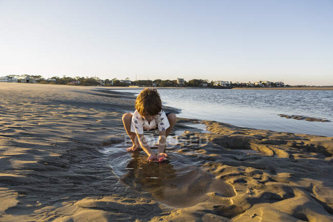 Six year old boy playing on the beach in a pool of water — Stock Photo
