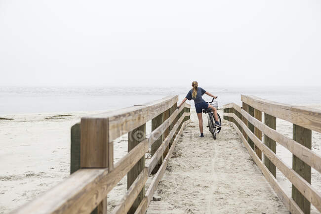 Teen menina ciclismo no arenoso praia pelo oceano, St. Simons Island, Geórgia — Fotografia de Stock